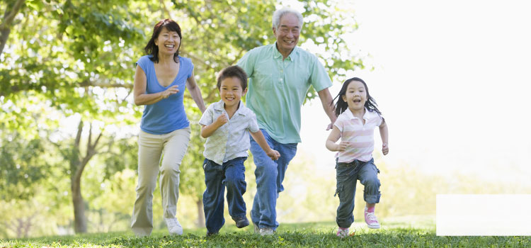 Se ve una familia asiática. La madre, el abuelo y dos niños caminan contentos por una pradera.