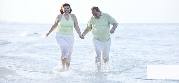Se ve una pareja corpulente de edad media. Dan un paseo por la playa. Saltando contentos por agua.